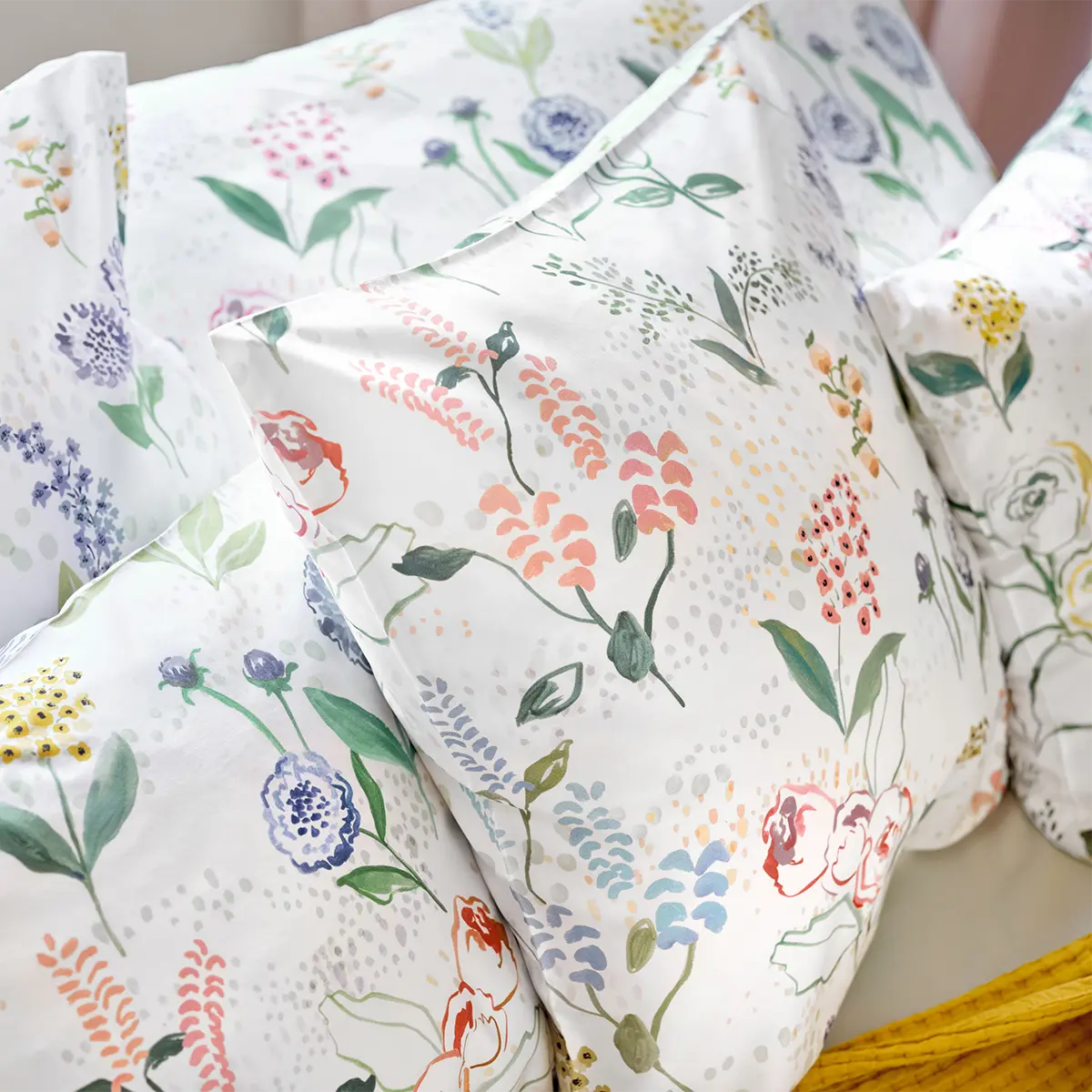 Bettwäsche Annika Kissenbezüge Nahaufnahme von Kissen mit weisser Bettwäsche und buntem Blumenmuster in verschiedenen Farben.