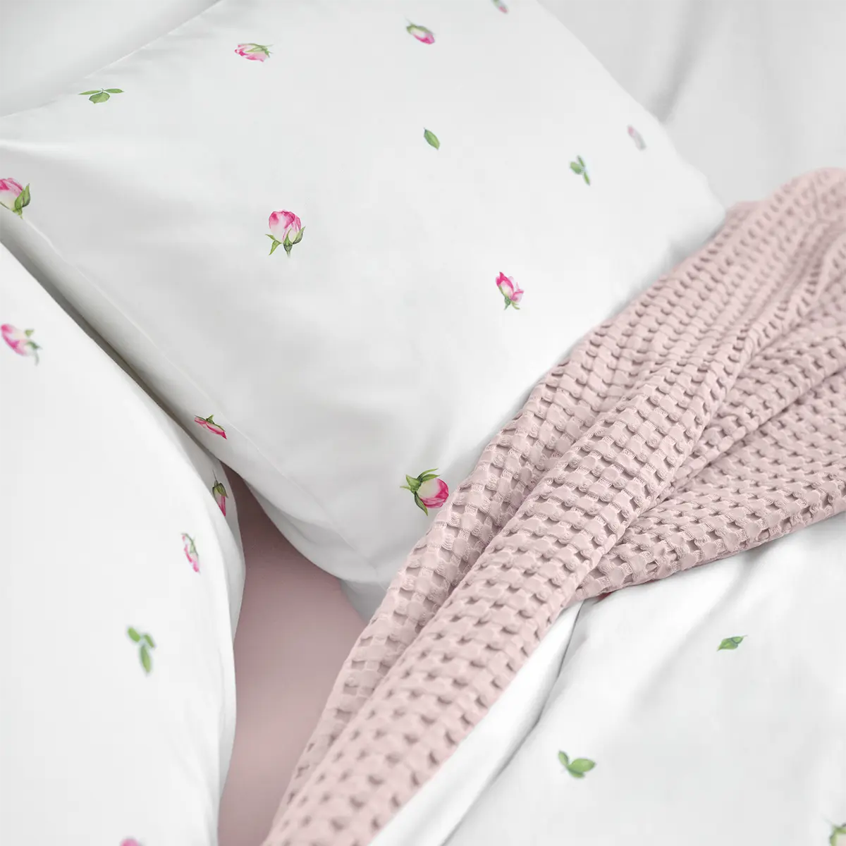 Nahaufnahme der Jeunesse-Bettwäsche, die mit kleinen rosa Blüten und grünen Blättern verziert ist, kombiniert mit einer weichen, rosa Decke.