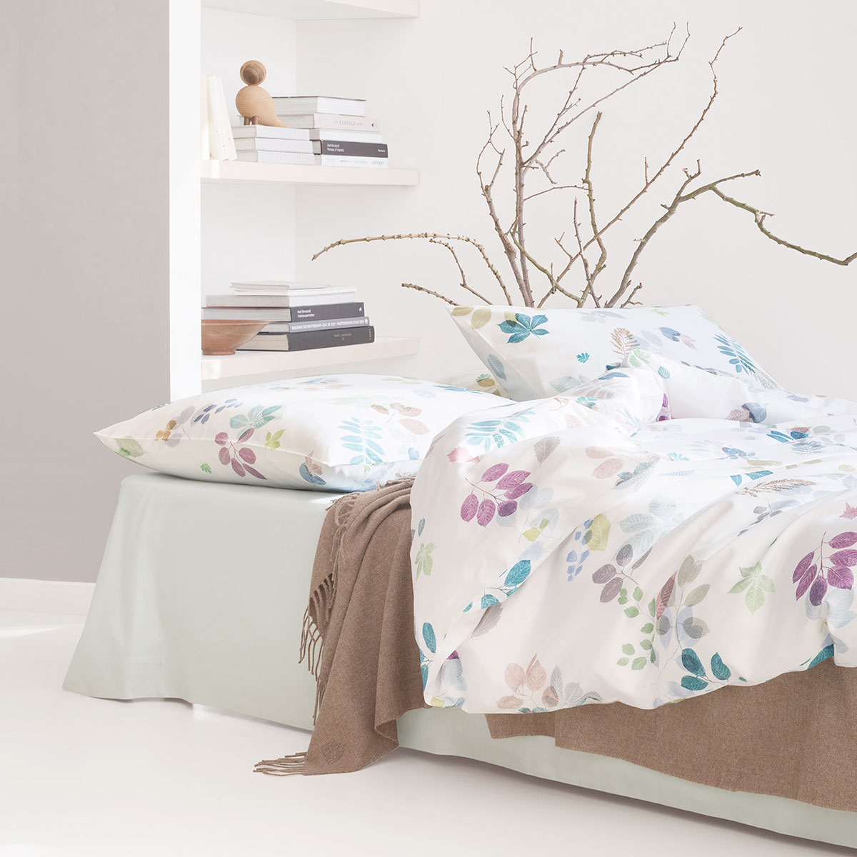 Schlafzimmer mit Eliv Bettwäsche Set, dekoriert mit Blättermuster in Pastellfarben, ergänzt durch neutrale Akzente und einen gemütlichen Zweig im Hintergrund.