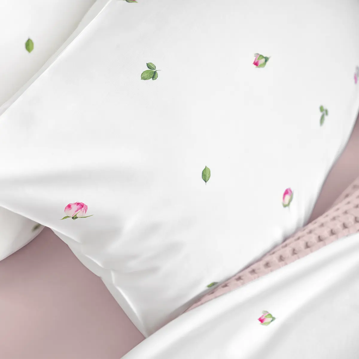 Weisse Kissen der Jeunesse-Bettwäsche, geschmückt mit rosa Blütenknospen und grünen Blättern, ideal für eine romantische Schlafzimmergestaltung.