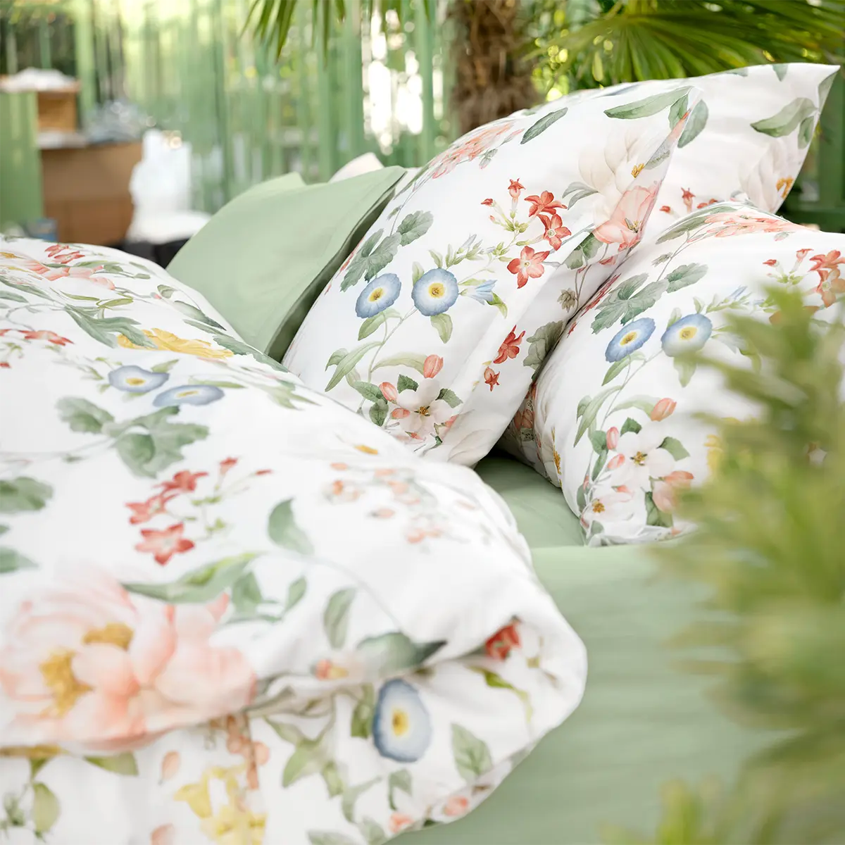 Bettwäsche Artemis mit farbenfrohem Blumenmuster und grünen Kissenbezügen in einem Garten.
