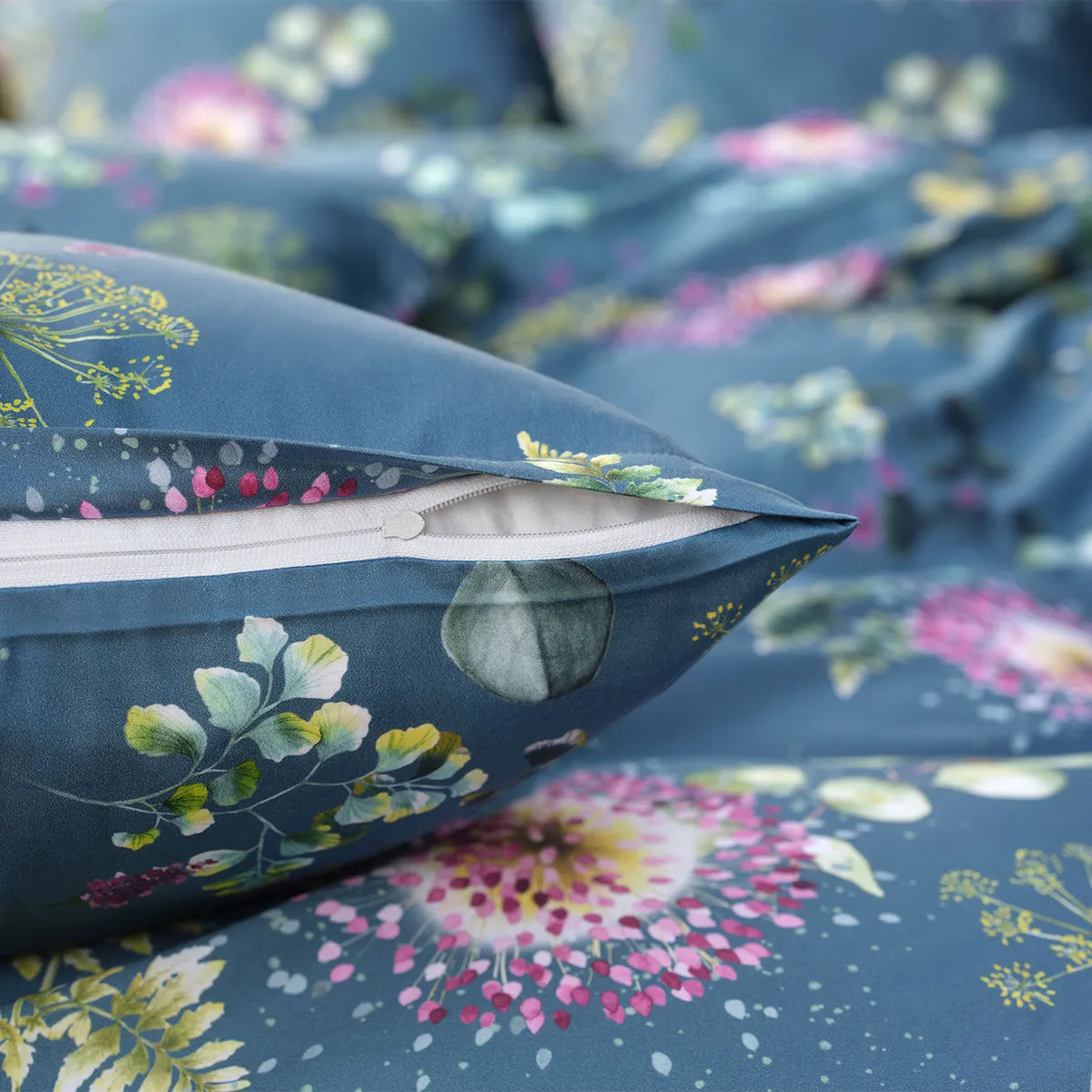 Nahaufnahme des Schlossberg Bettwäsche Nele Kissenbezugs mit elegant verdecktem Reißverschluss. Das detailreiche florale Muster in Pink, Grün und Gelb auf tiefblauem Stoff kombiniert luxuriöse Optik mit funktionaler Raffinesse.
