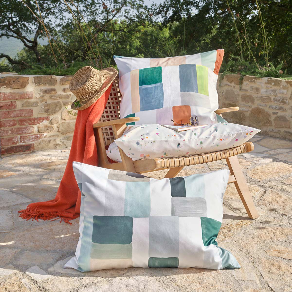 Mika Kissen im Outdoor-Bereich Zwei Kissen mit geometrischem Muster in sanften Farbtönen, drapiert auf einem Holzstuhl im Garten.