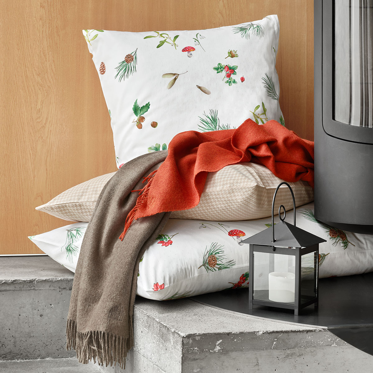 Dekoratives Kissen Hazel mit Waldmuster Kissen Hazel mit Waldmuster neben einem roten Schal und einer Laterne, ideal für eine gemütliche Atmosphäre.
