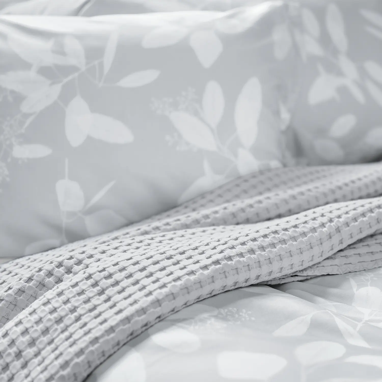 Detailansicht der grauen Omeo Bettwäsche mit weissem Blättermotiv, kombiniert mit einer grauen Decke.