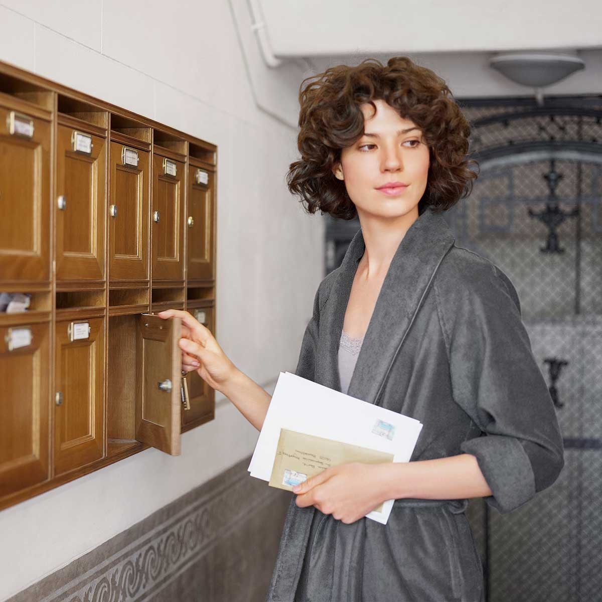 Eine Frau trägt einen grauen Bademantel aus der Schlossberg-Kollektion und holt Post aus ihrem Briefkasten.