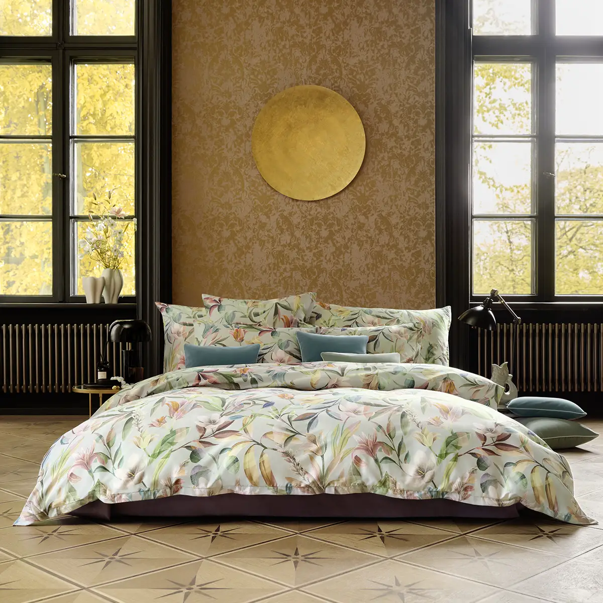 Ein Schlafzimmer mit Schlossberg Bettwäsche im Adele Design, das florale Muster in sanften Farben zeigt. Kissen in verschiedenen Größen und Farben sind auf dem Bett arrangiert, vor einem großen Fenster mit Herbstblick.