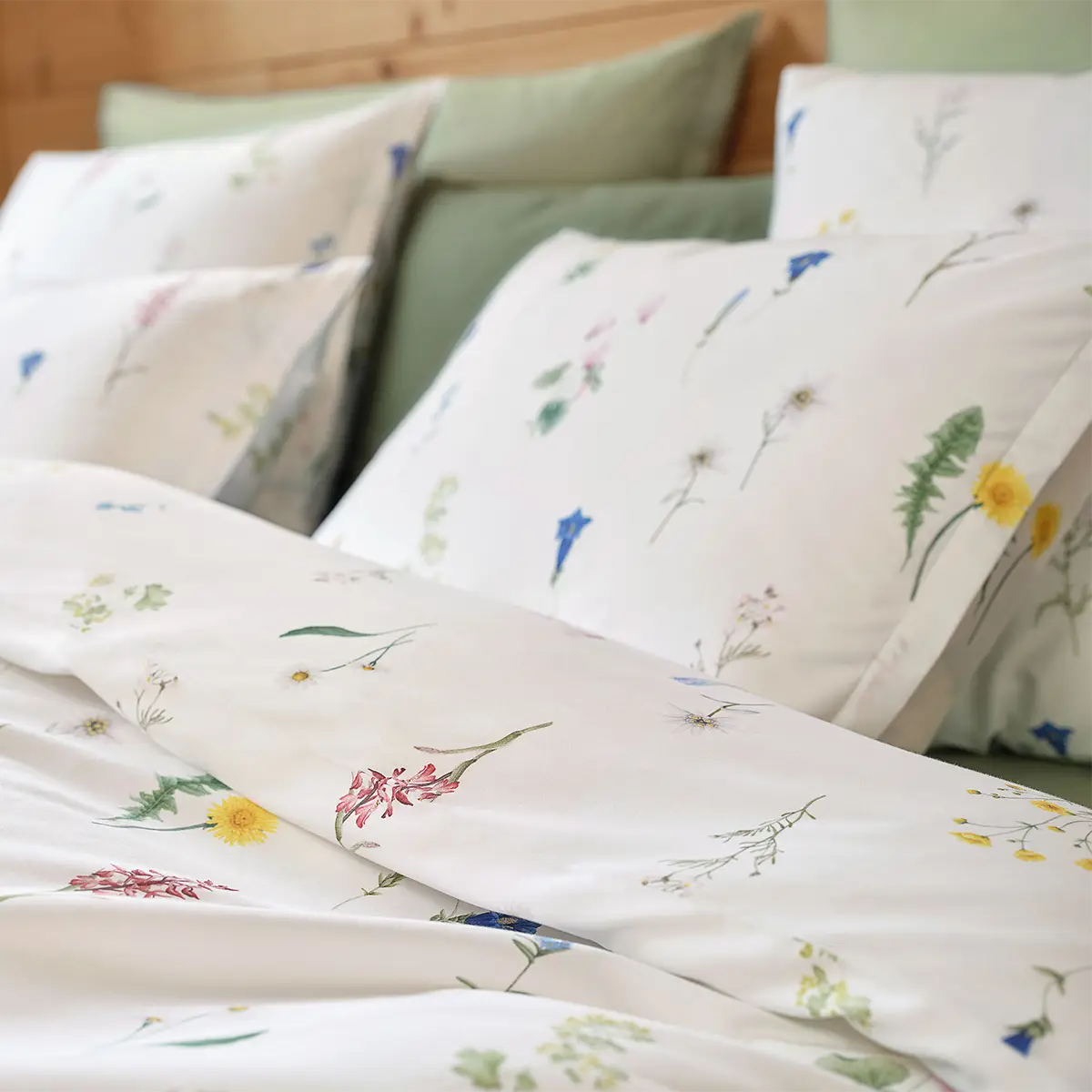 Detailansicht der Bettwäsche "Flurina" mit floralen Mustern Nahaufnahme der weissen Bettwäsche "Flurina", die verschiedene Blumenmotive zeigt, kombiniert mit grünen Dekokissen.