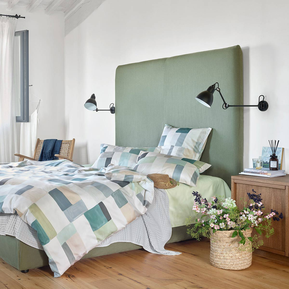 Schlafzimmer mit Mika Bettwäsche Schlafzimmer mit einem Bett, das mit der Mika Bettwäsche in geometrischem Design bezogen ist, daneben ein Nachttisch mit Blumen.
