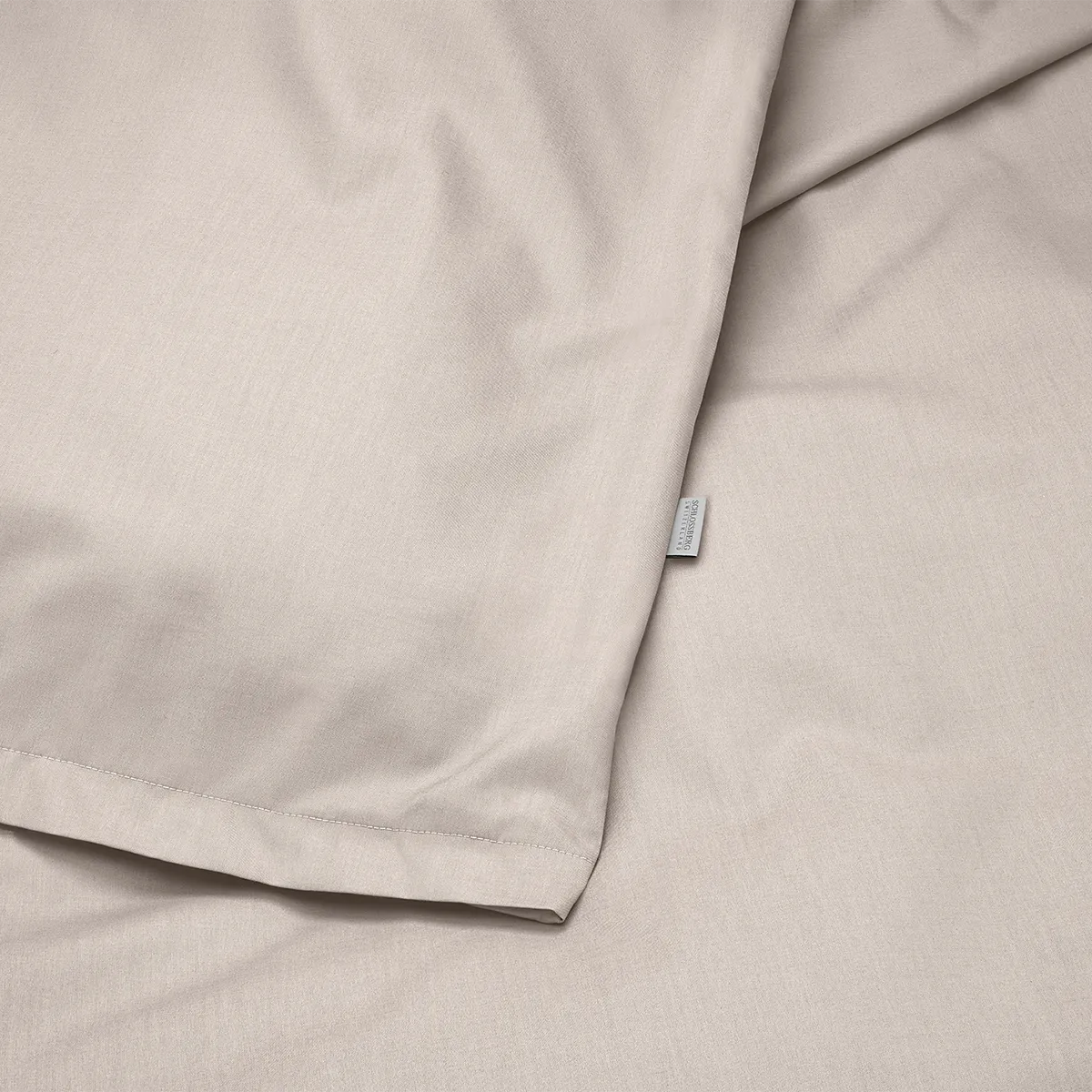 Nahaufnahme der Schlossberg Bettwäsche Ben in der Farbe Sand. Der hochwertige Stoff präsentiert sich in einer feinen, natürlichen Textur mit dezenter Webstruktur und einem kleinen Schlossberg-Label.