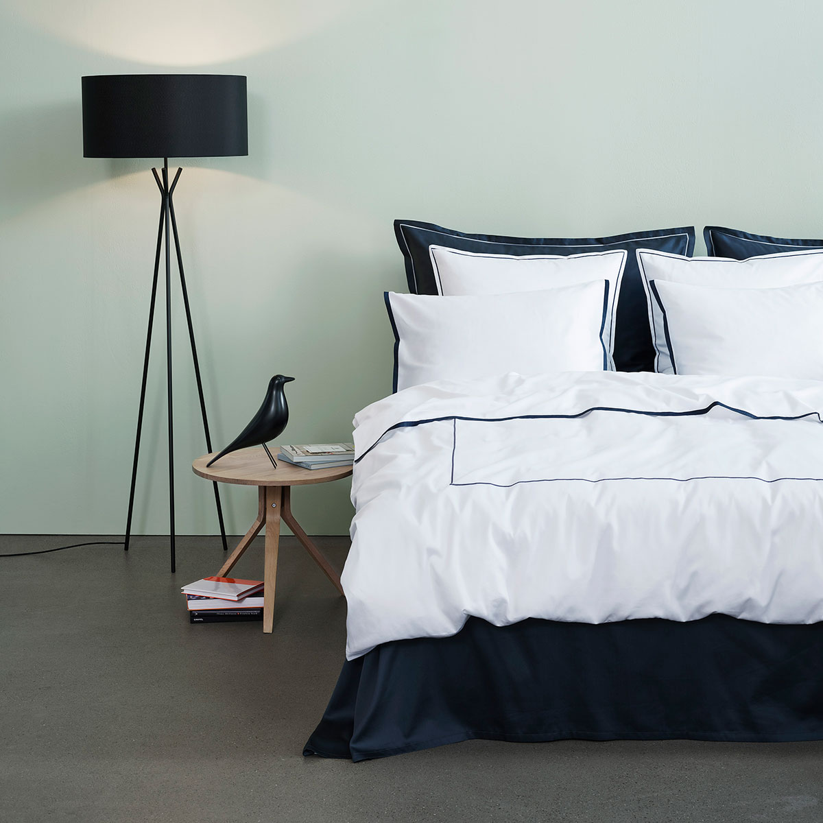 Ein modernes Schlafzimmer mit einem Bett, das mit der dunkelblauen und weissen Bettwäsche Clark bezogen ist. Ein stilvolles Nachttischchen und eine Stehlampe runden das Bild ab.