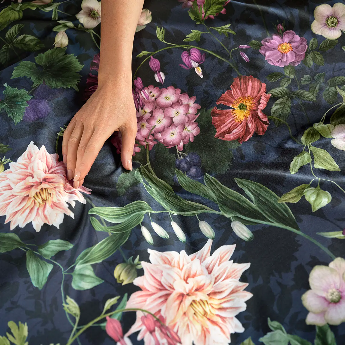 Detailansicht der Ophelia Bettwäsche Eine Hand berührt den weichen Stoff der Ophelia Bettwäsche, die mit einem detailreichen, floralen Muster in kräftigen Farben gestaltet ist.