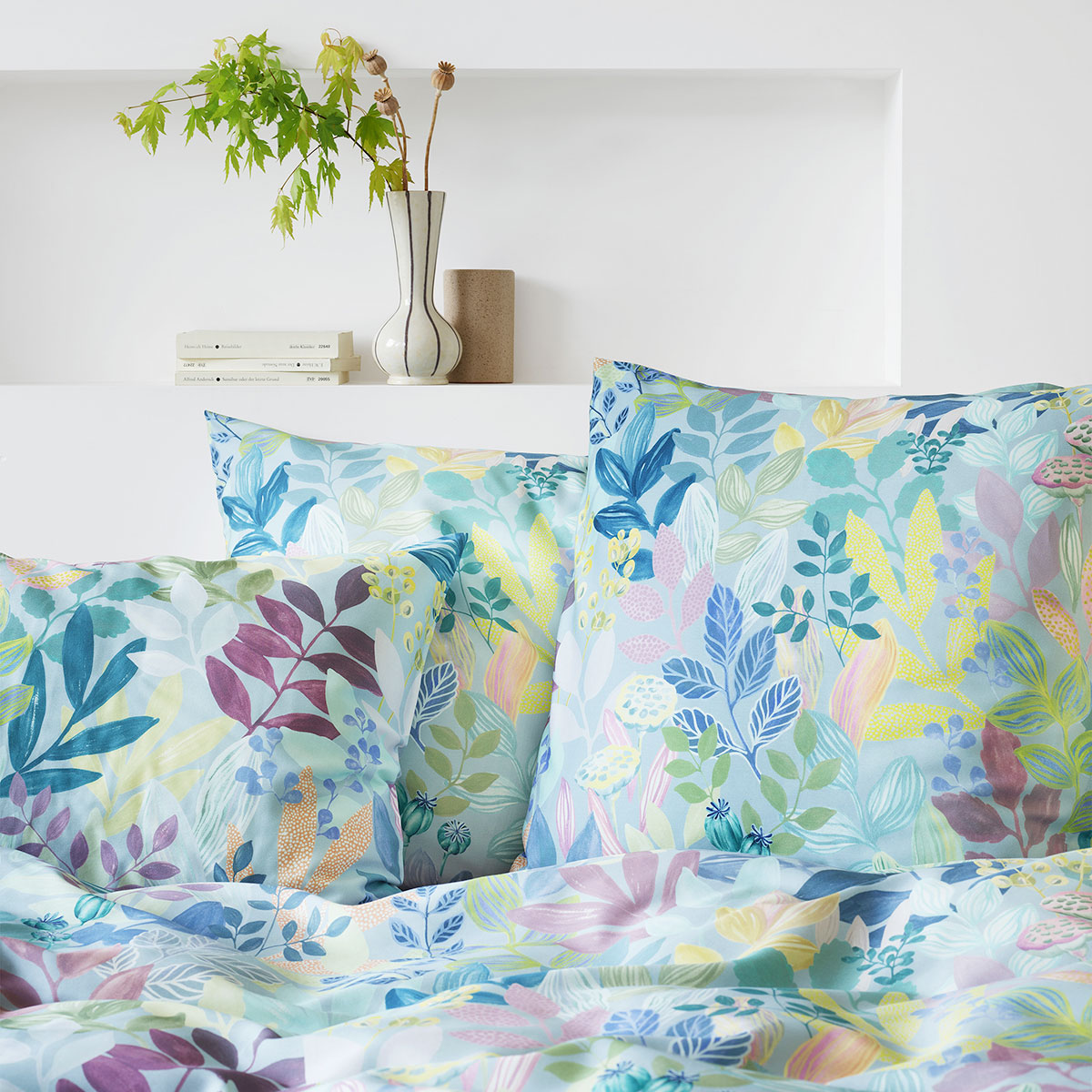 Kopfkissen mit Blättermuster - Bettwäsche "Frida" Kopfkissen aus der Bettwäsche "Frida" mit einem lebhaften Blättermuster in einem modernen Schlafzimmer, dekoriert mit einer Vase und Pflanzen.