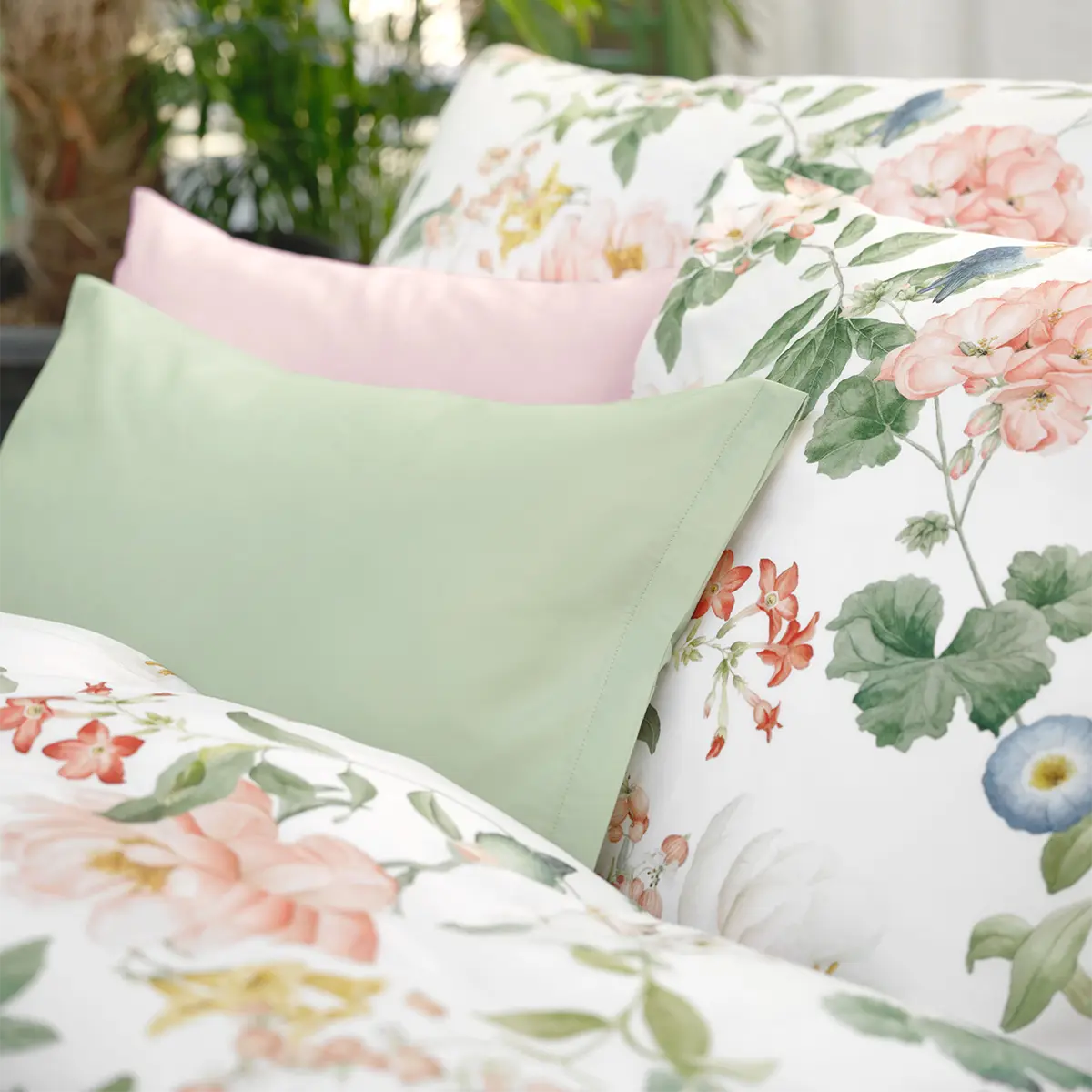 Bettwäsche Artemis mit bunten Blumen und grünen Kissen Bettwäsche Artemis mit farbenfrohen Blumendrucken und grünen Kissenbezügen auf einem Bett.