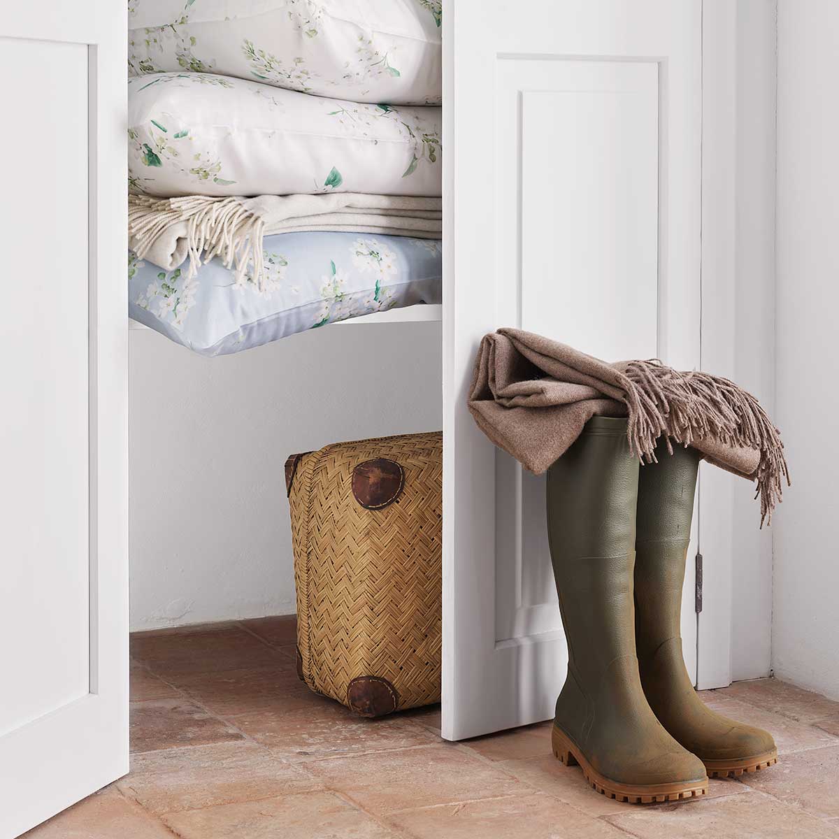 Gestapelte Bettwäsche May mit floralem Muster in einem Schrank, kombiniert mit anderen Textilien und dekorativen Elementen.