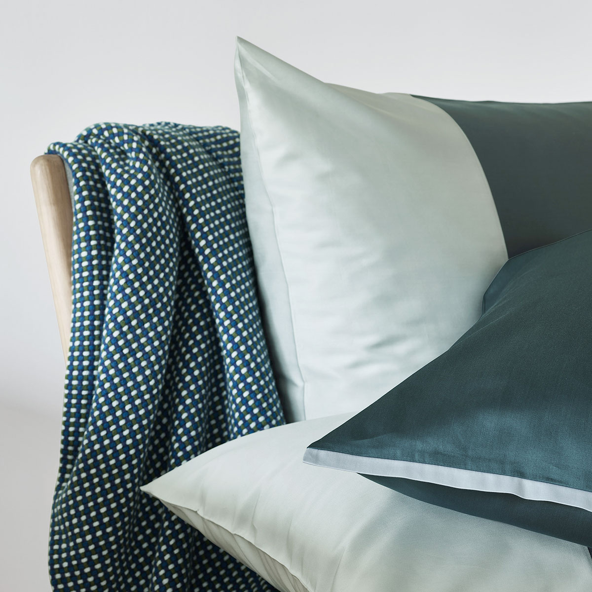 Bettwäsche Allen mit gemusterter Decke Nahaufnahme von weissen und dunkelgrünen Kissen, die auf einem Stuhl mit einer blau-weiss gemusterten Decke liegen.