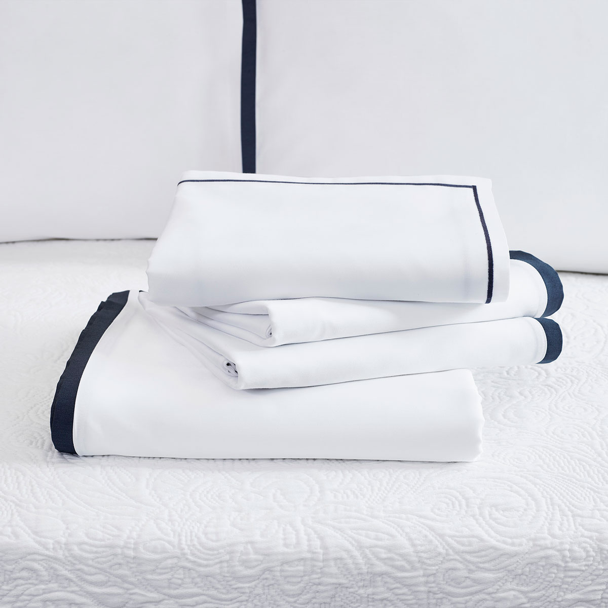 Stapel weisse Bettwäsche Clark mit dunklem Rand Ein Stapel der Bettwäsche Clark in weiss mit dunklem Rand, auf einem Bett drapiert.