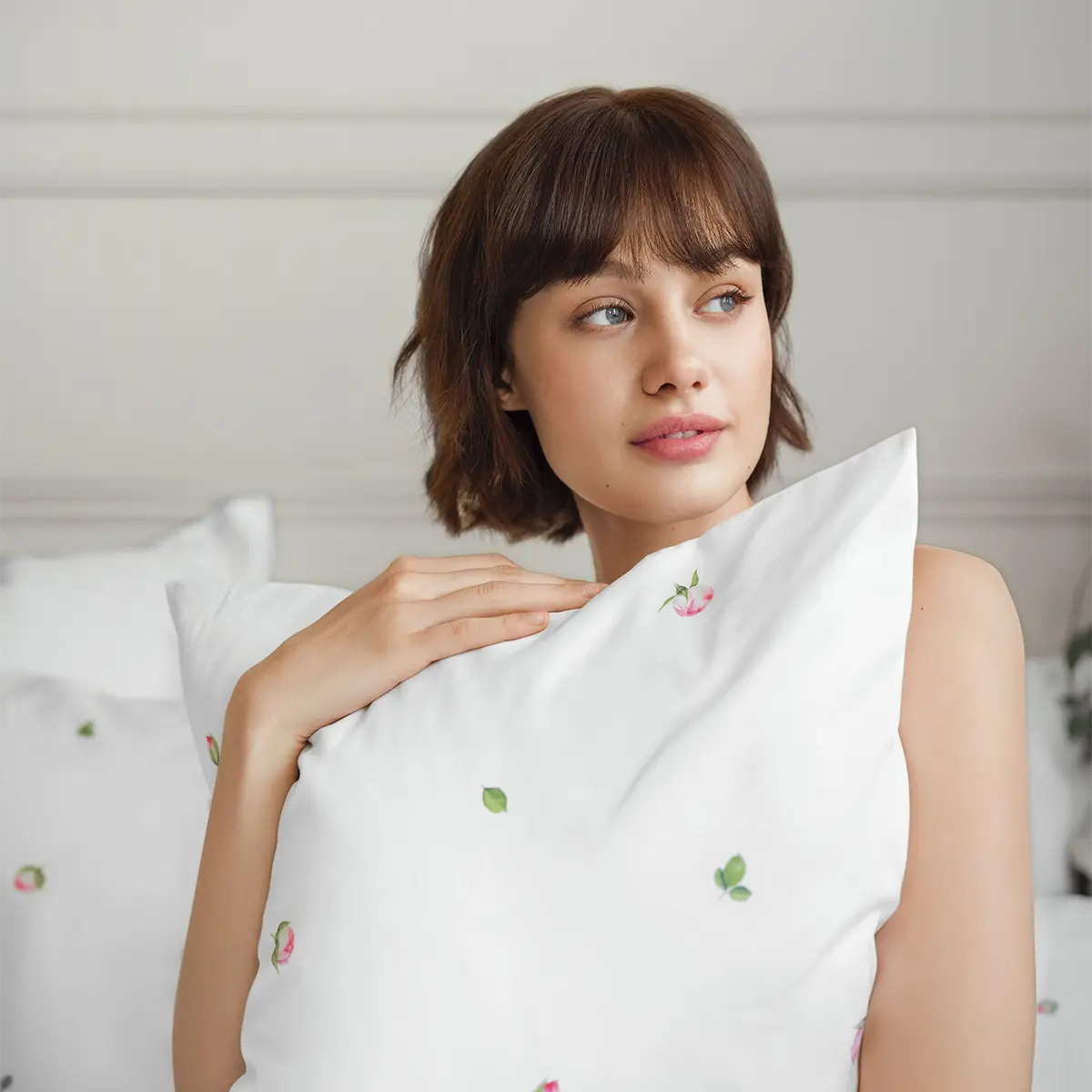 Jeunesse-Bettwäsche für einen sanften Start in den Tag Eine Frau kuschelt sich in die Jeunesse-Bettwäsche, die mit zarten rosa Blüten verziert ist, und geniesst einen ruhigen Moment.