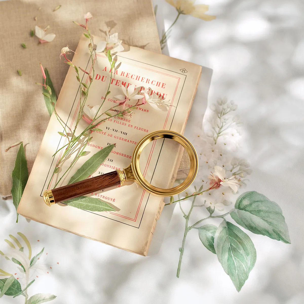 Schlossberg Bettwäsche Zinnia – Detailaufnahme mit stilvoller Dekoration Stimmungsvolle Nahaufnahme der Schlossberg Bettwäsche Zinnia mit einem floralen Muster aus filigranen Blüten und grünen Blättern auf weißem Stoff. Eine antike Lupe mit goldenem Rahmen und Holzgriff liegt auf einem klassischen französischen Buch.