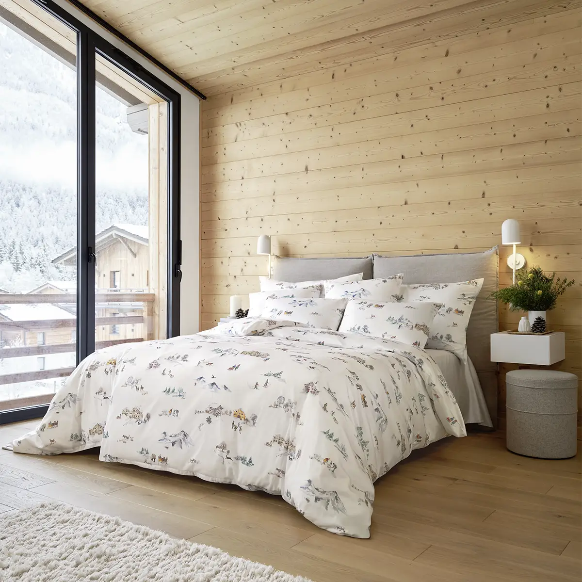 Schlafzimmer mit einer grossen Fensterfront und der Montagne Bettwäsche, die eine winterliche Berglandschaft darstellt.
