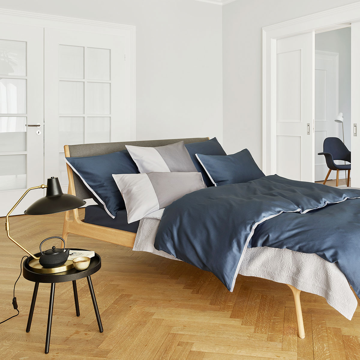 Elegantes Schlafzimmer mit Bettwäsche Clark in dunkelblau und weiss Ein elegantes Schlafzimmer mit einem Bett, das mit der dunkelblauen und weissen Bettwäsche Clark bezogen ist. Ein stylischer Nachttisch und Accessoires ergänzen das Ambiente.