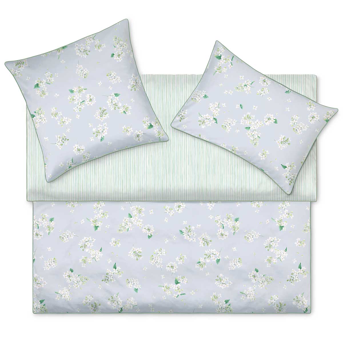Bettwäsche April floral und gestreift Ein Bett mit der Bettwäsche April, die ein florales Muster und grüne Streifen zeigt. Die Kissen und Decken sind hellblau mit weissen Blüten.