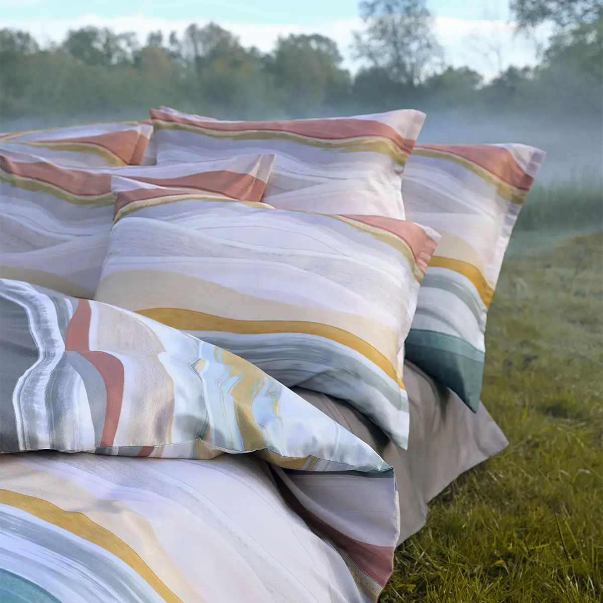Linus Bettwäsche Set in natürlicher Umgebung Bett mit mehreren Kissen und Decke der Linus Bettwäsche, aufgestellt in einer natürlichen, nebligen Umgebung.