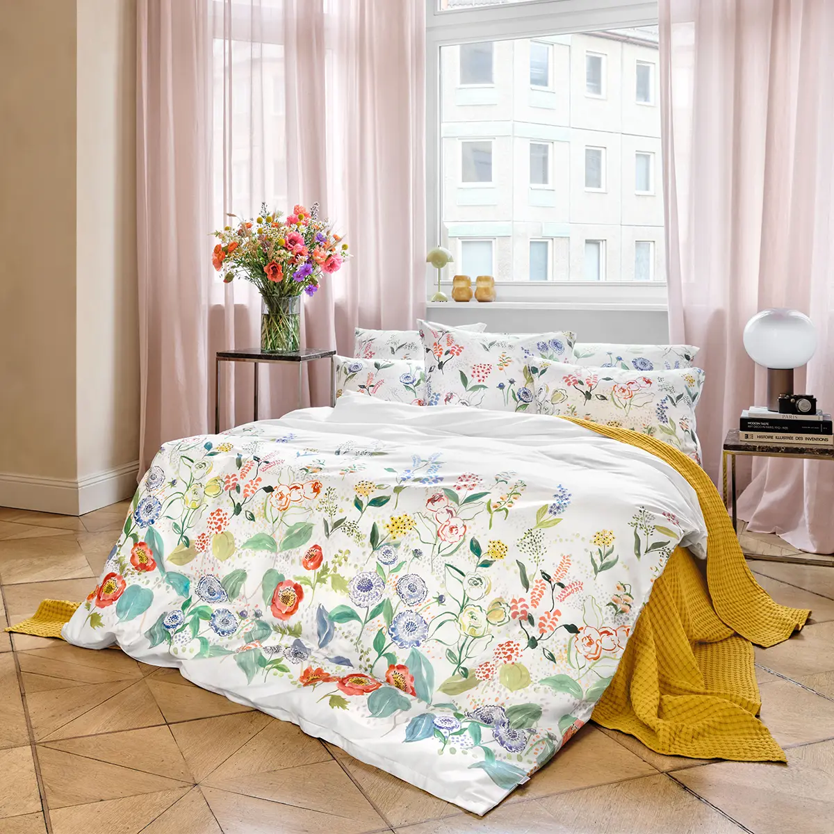 Bettwäsche Annika im stilvollen Schlafzimmer Ein stilvolles Schlafzimmer mit einem Bett, das mit weisser Bettwäsche und floralem Muster bezogen ist. Neben dem Bett steht ein Blumenstrauss in einer Vase.