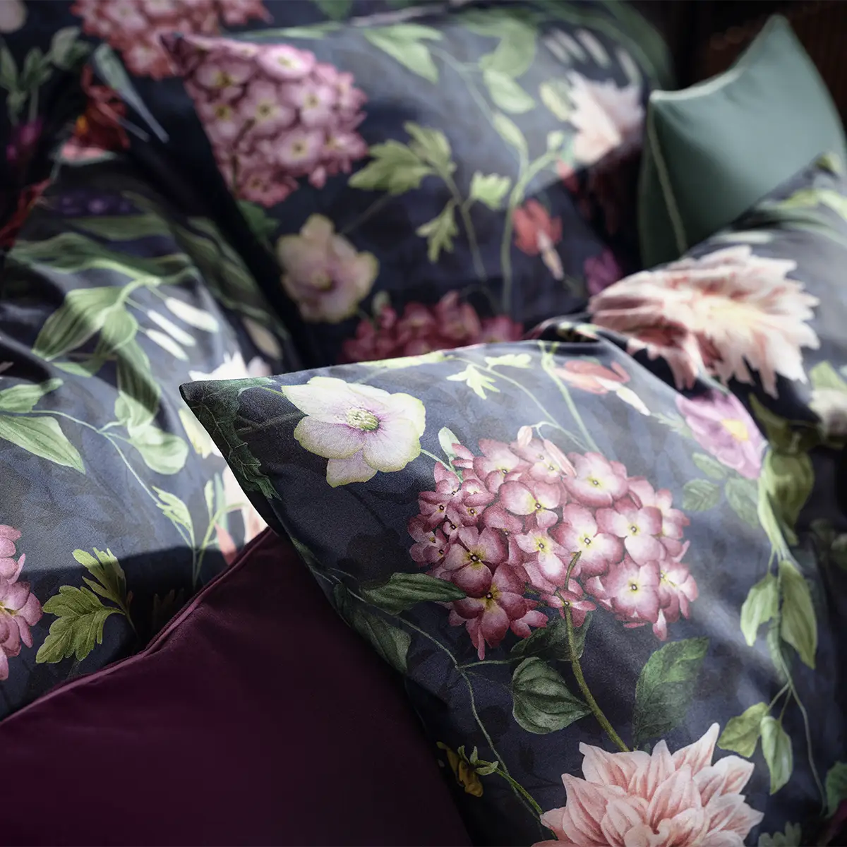 Ophelia Kopfkissen in Dunklen Farben Nahaufnahme eines Kopfkissens mit dem dunkelblauen, floralen Muster der Ophelia Bettwäsche, das zarte Blüten in Violett und Rosa zeigt.