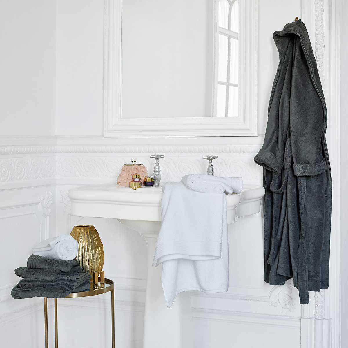 Schlossberg Frottier Coshmere im Badezimmer Ein Badezimmer mit einem grauen Schlossberg Frottier Coshmere Bademantel an einem Haken, weissen Handtüchern auf einem Tisch und weiteren Pflegeprodukten.