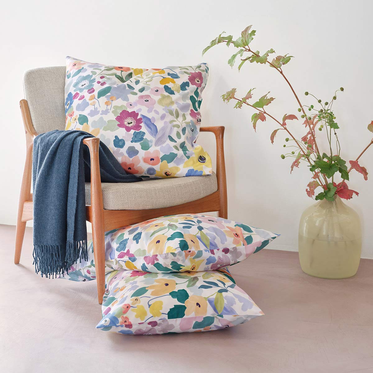 Kissen in der Bettwäsche "Hanna" mit buntem Blumenmuster, dekorativ auf einem Stuhl arrangiert.